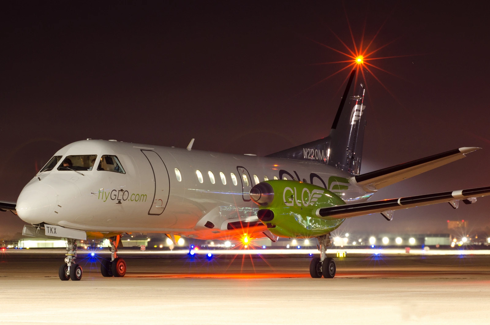 A GLO Saab aircraft on the apron at night, wearing the green and gray airline livery